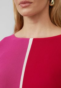 Aansluitende top met een kleurblokontwerp in tinten roze en rood, met een witte verticale streep. De stof is een gestructureerde brei.