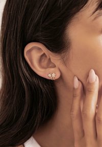 Gold-colored star-shaped earrings with sparkling accents, featuring a smooth finish, worn in the ear. Subtle design emphasizes elegance.