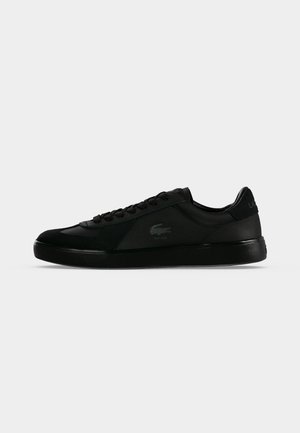 Baskets basses noires à lacets, semelle texturée et logo discret sur le côté et le talon, présentées sur un fond clair uni.