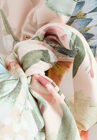 Tissu doux noué avec un motif floral dans des nuances pastel de rose, vert, bleu et jaune.