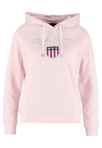 Jasnoróżowa bluza z kapturem z kieszenią kangurką, regulowanym kapturem i haftowanym logo GANT. Z przodu znajduje się tarcza z czerwonymi i niebieskimi akcentami.