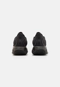 Sorte atletiske sko med en glat stofoverdel, struktureret hæl og flexibelt gummisål. Rundet form med minimale design detaljer.
