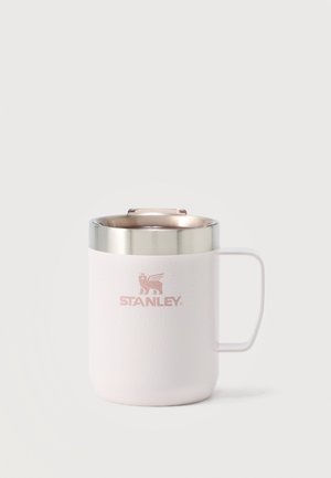 Tasse isotherme Stanley blanche avec un bord et une poignée argentés, ornée d'un logo de lion aux ailes roses et munie d'un couvercle sur le dessus.