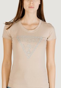 T-shirt beige aderente a maniche corte, con un design del logo triangolare in argento e decorazioni sulla parte anteriore. Materiale in cotone morbido.