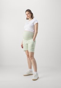 Hvit kortermet topp og grønne stripete shorts. Shortsene er knelange med sidelommer. Skoene er hvite med brune såler.