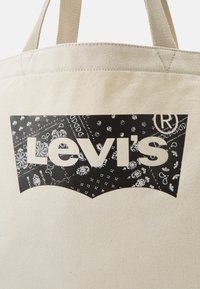 Torba na ramię z płótna z wyraźnym czarnym logo Levi's oraz wzorem w stylu bandany, na tle naturalnego beżowego koloru.