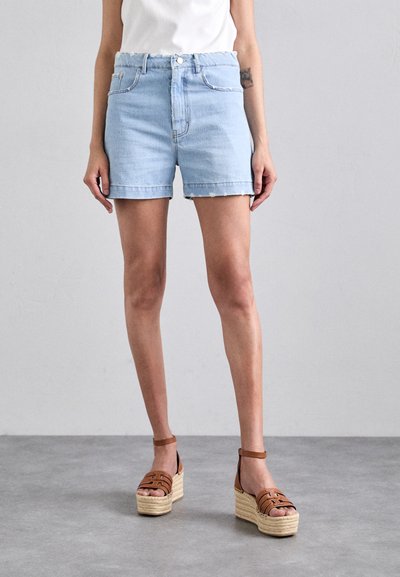 Shorts en denim bleu clair avec un ourlet effiloché, dotés de poches avant et d'une coupe décontractée. Associés à des sandales compensées marron.
