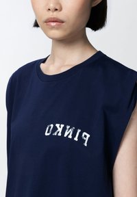 Tamna plava bezrukavna pamučna majica s bijelim izblijedjelim logom 'PINKO' sprijeda, okruglim izrezom i mekanom teksturom.