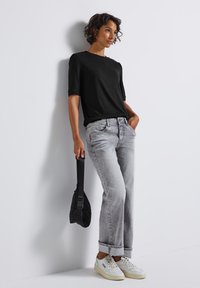 Sort kortærmet topp, lysegrå jeans med opfoldede manchetter, hvide sneakers og en sort kviltet taske. Enkelt design med en afslappet pasform.