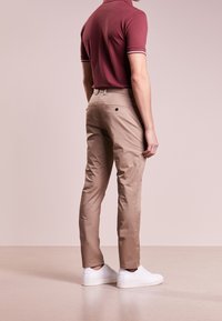 Pantaloni chino beige con una vestibilità slim, dotati di tasca posteriore e una texture liscia. Abbinati a una polo bordeaux e scarpe da ginnastica bianche.