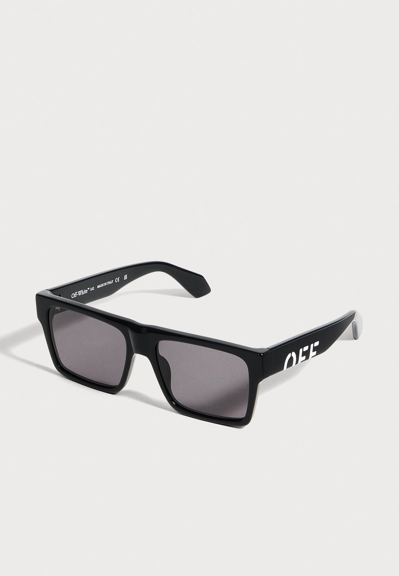 Lunettes de soleil rectangulaires noires avec des verres foncés et le logo blanc « OFF » sur des branches épaisses, présentées sur un fond clair uni.