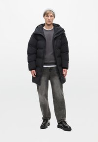 Černý puffa kabát s kapucí, šedá mikina a vybledlé černé džíny. Nosené s černými botami a světle šedou čepicí. Minimalistický design.