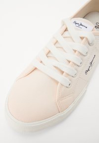 Sneaker in tela rosa chiaro con lacci bianchi, punta arrotondata e suola in gomma testurizzata. Presenta un dettaglio con logo sul lato.