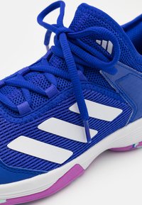 Scarpa sportiva blu realizzata in mesh e materiale sintetico. Presenta strisce bianche, parte superiore testurizzata e una suola bicolore con dettagli rosa.