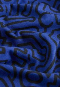 Zils audums ar gludu tekstūru, ar kontrastējošu melnu abstraktu līniju un formu rakstu, radot dinamisku vizuālo efektu.