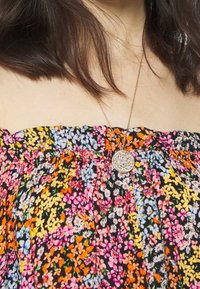 Bloemig patroon op een stoftop met een zwarte achtergrond, versierd met kleurrijke bloemen in oranje, roze en blauw; een zilveren ketting met een ronde hanger.