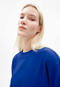 Sweatshirt bleu à col rond avec une finition texturée et un logo brodé. Tissu lisse, coupe décontractée et manches courtes.