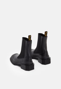 Svarta läderankelboots med elastiska sidopaneler, klackar med blockdesign och gula dragflikar baktill. Slät textur och rund tådesign.