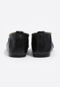 Czarne skórzane buty na płaskiej podeszwie z zaokrąglonym noskiem, ozdobione srebrnym zamkiem błyskawicznym wzdłuż górnej krawędzi oraz przeszyciami.