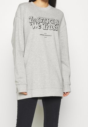 Felpa grigia oversize in cotone, con testo grafico nero "In GIRLS We Trust" e "ARMANI EXCHANGE" stampato sul davanti.