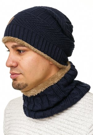 Navy knit beanie with textured patterns and beige faux fur lining; paired with a matching neck warmer in the same color and texture.
