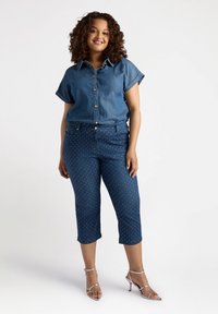 Camisa de denim con mangas cortas enrolladas, frente abotonado; jeans cortos de lunares; tacones plateados con tiras; texturas suaves, color azul oscuro.