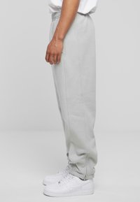 Hellgraue Sweatpants mit elastischem Bund und seitlichen Reißverschlusstaschen, kombiniert mit weißen Turnschuhen. Glatte Textur und schmal zulaufender Schnitt.