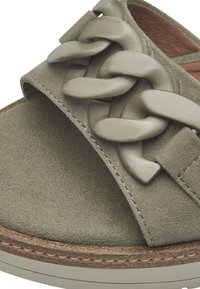 Des sandales en daim vert présentent une large bride avec un design en tresse, une semelle intérieure beige texturée et une semelle ronde avec des coutures contrastées.