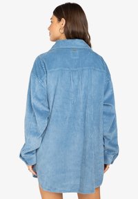 Giacca camicia in corduroy blu chiaro con colletto a punta, maniche lunghe e texture a righe verticali, caratterizzata da un retro con yoke e una vestibilità rilassata.