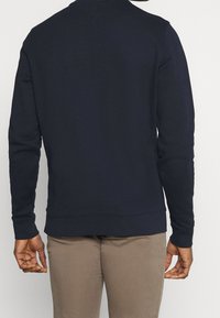 Felpa navy con maniche lunghe e polsini a coste. Tessuto morbido, vestibilità regolare, con orlo arrotondato e un sottile dettaglio cucito sul retro.