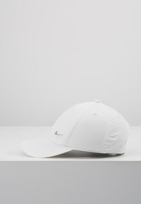 Fehér baseball sapka puha anyagból, enyhén ívelt napernyővel, varrott díszítéssel és ezüst logóval az elején.