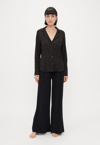 Camisa preta com padrão de onça, de botões e colarinho, combinada com calças largas pretas. Tecido suave, corte descontraído e detalhes mínimos.