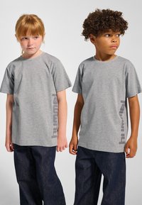 Grå T-shirts med korta ärmar har en subtil textur och en kontrasterande "hummel"-logotyp tryckt vertikalt i en mörkare grå nyans. Bärs med mörka jeans.