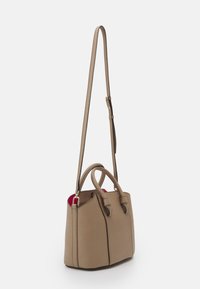 Vaaleanruskea käsilaukku, jossa on teksturoitu pinta, kaksinkertaiset yläkahvat ja pitkä säädettävä hihna. Sisätila esittelee kontrastina olevan punaisen vuoren.