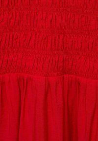 Robe rouge avec corsage smocké et jupe froncée, dotée d'un tissu texturé avec des plis verticaux et horizontaux. Aucun accent supplémentaire visible.