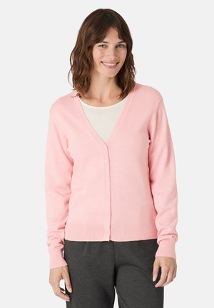 Cardigan rose clair avec un col en V, des manches longues et une fermeture à boutons. Texture douce, ourlet et poignets côtelés, porté sur un haut crème et un pantalon gris.