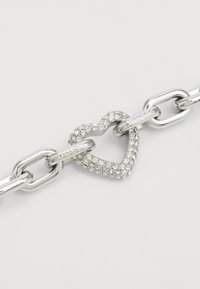 Bracciale in argento con catena, dotato di una chiusura a forma di cuore arricchita con strass trasparenti, con la scritta "GUESS" incisa sui link.