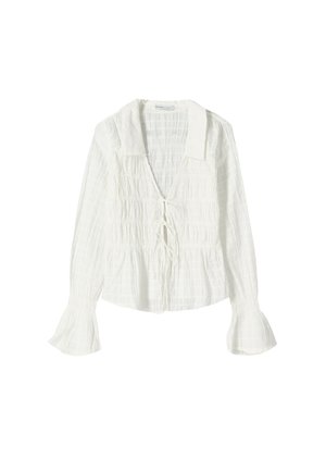 Blouse blanche à manches longues avec tissu froncé, large col, liens à l'avant et poignets évasés sur un fond uni.