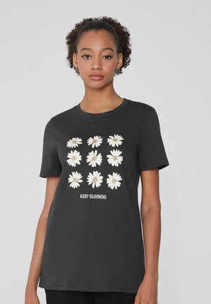 Camiseta de algodón negra con un gráfico de margarita en blanco y beige con el texto "SIGUE FLORANDO" en blanco, cuello redondo y mangas cortas.
