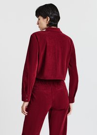 Giacca corta in velluto a coste rosso con maniche lunghe e polsini con bottoni, abbinata a pantaloni a vita alta coordinati con tasche.