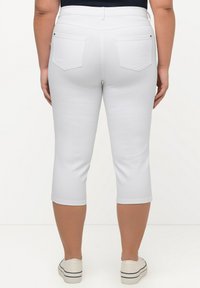 Pantalones capri blancos con un diseño ajustado, cintura media, bolsillos traseros y una textura suave, combinados con zapatillas blancas informales.
