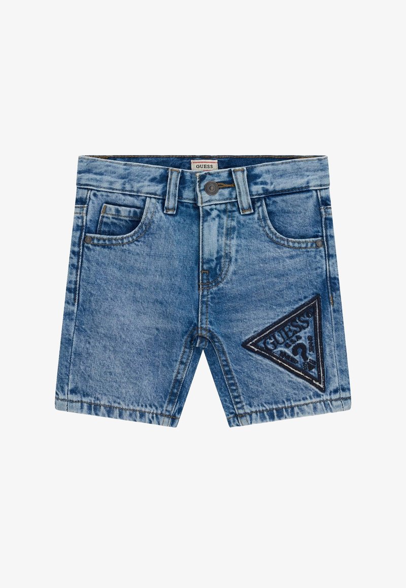 Shorts en denim bleu avec poches avant, passants pour ceinture, fermeture par boutons, et un écusson triangulaire du logo Guess sur la jambe droite.