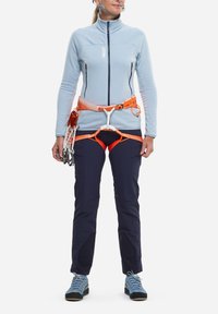 Hellblaues Zip-up-Fleece, orange Harness mit Gear-Schlaufen, marineblaue Hose mit Cargo-Taschen und blaue Kletterschuhe mit schwarzen Sohlen.