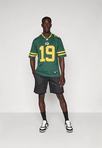 Zaļš futbola krekls ar dzeltenām svītrām, numurs 19 un logo. Kopā ar melnām sieta šortiem un melni baltām sporta kurpēm.