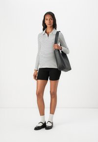 Randig långärmad polo skjorta i vit och marin, svarta shorts och svart handväska. Modellen har vita strumpor och svarta skor med spänne.