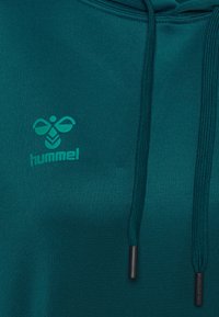 Bluza z kapturem w kolorze zielonkawoniebieskim z logo hummel na piersi, wyposażona w dwa zielonkawoniebieskie sznurki z czarnymi plastikowymi końcówkami.