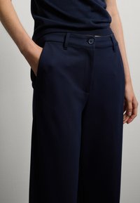 Pantaloni navy realizzati in tessuto liscio, dotati di chiusura a bottone, tasche laterali e una vestibilità rilassata con vita su misura.