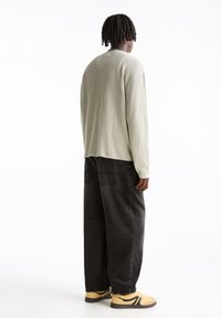 Hellgrüner Rippenstrickpullover mit lockerem Schnitt, kombiniert mit schwarzen Jeans in weiter Passform und gelben Sneakers mit schwarzen Akzenten.