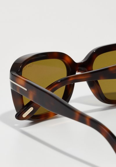 Schildpatt-Sonnenbrille mit gelben Gläsern, dickem Acetatrahmen und Metallelementen. Sie verfügt über eine markante, übergroße Form und gebogene Bügel.