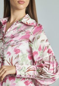 Blusa floreale in tonalità di rosa e verde, con colletto, chiusura a bottoni frontalmente e maniche puff con polsini arricciati.